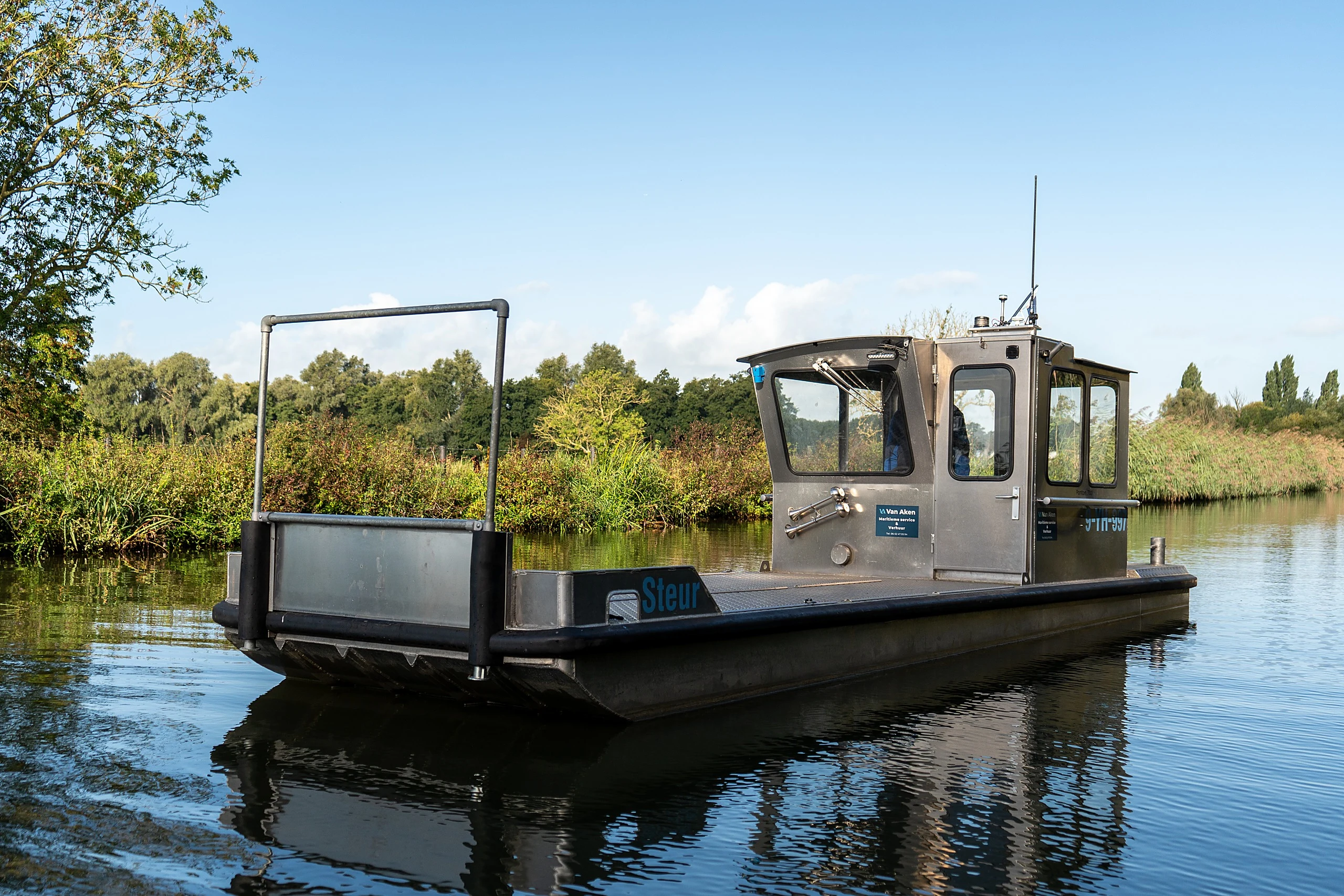 Werkboot Steur van opzij op een rustige vaart, met open laaddek, stuurhuis en buitenboordmotor